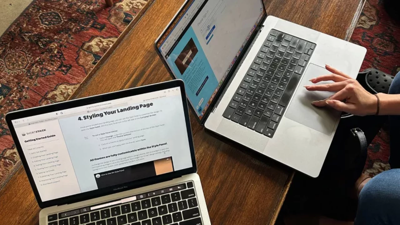 Two laptops on a wooden table with one showing a guide on styling a landing page and the other displaying a project in progress, capturing a workspace setup for web design or digital marketing.
